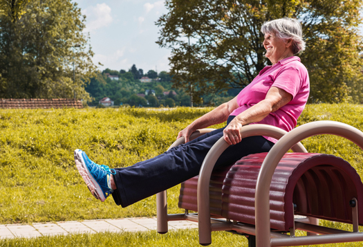 Smiling old woman doing balance exercises on sports equipment at the outdoor gym.