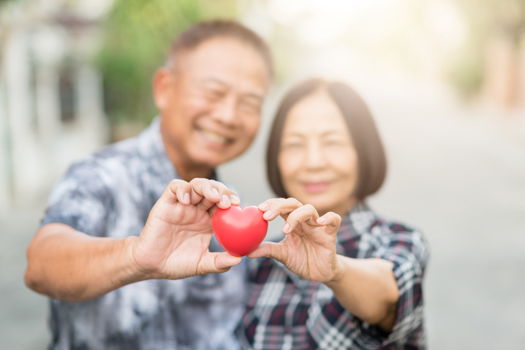 Happy senior Asian couple smiling while holding heart together outdoor. Selective focus on heart.