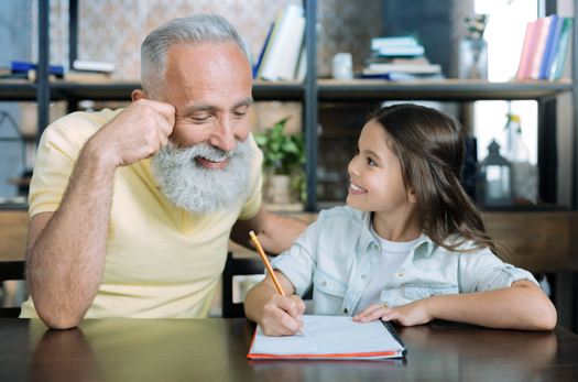Did you know. Joyful senior gentleman smiling while listening to his granddaughter and focusing his attention on a page of her notebook.