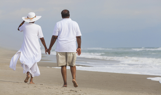 Happy romantic senior African American man and woman couple walking holding hands on a deserted tropical beach