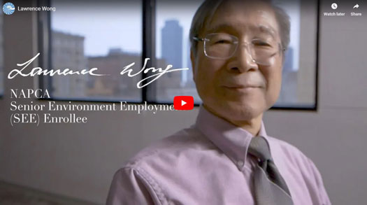 photo of Lawrence Wong, a NAPCA Senior Environmental Employment program participant, wearing a tie, with a city skyline outside the window behind him