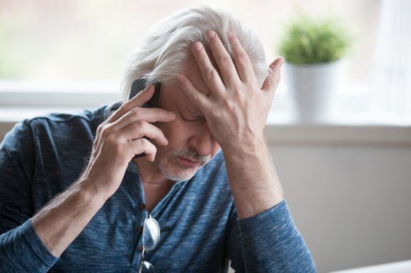 concerned man restying his head on his hand while talking on the phone