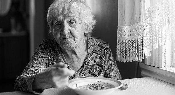 elderly woman eating soup in front of a window