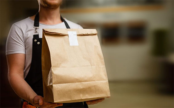 close-up photo of a food delivery person holding paper bag of food