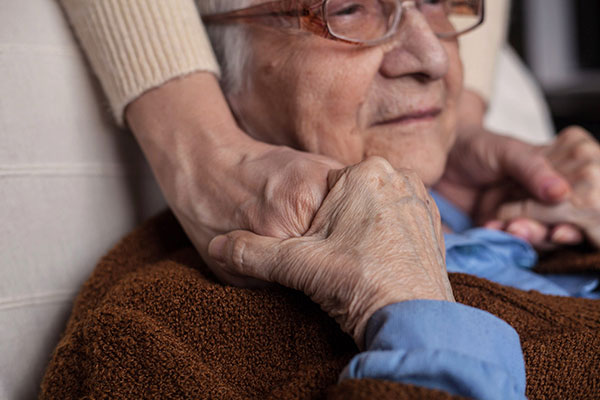 elderly woman resting her hands on husband's shoulders