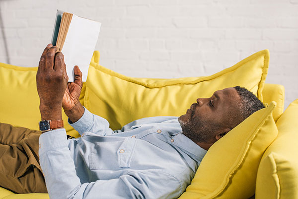 man reading a book while laying on a couch