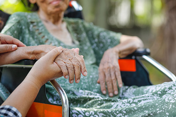 woman in wheelchair holding her caregiver's hand