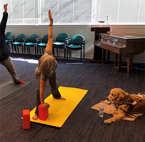 Camille practicing yoga on a mat designed for those with vision loss. Camille’s guide dog sits nearby.