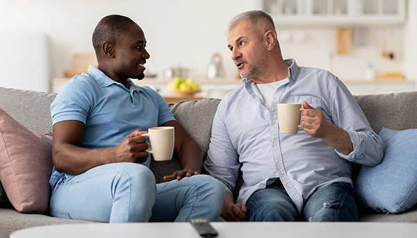 two men talking and drinking coffee on a couch