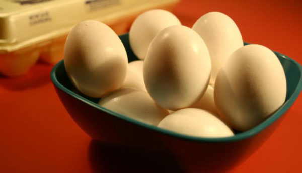 a green bowl full of hard boiled eggs on a red table