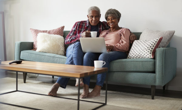 Senior Couple Sitting On Sofa At Home Using Laptop To Shop Online