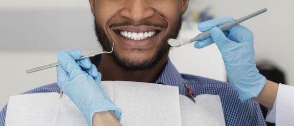 Cropped of stomatologist hands in protective gloves with tools and smiling patient black man, panorama
