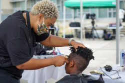 A black man gives his son a haircut at an outdoor event.