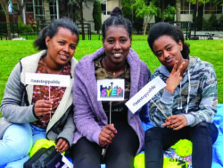 three SYEP youth sitting on a green lawn holding SYEP signs