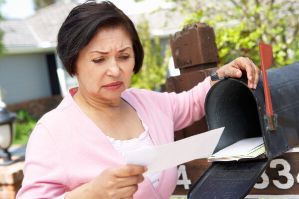 Worried Senior Hispanic Woman in pink cardigan Checking Mailbox