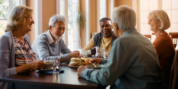 Group of senior people enjoying in conversation during lunch at dining table at nursing home.