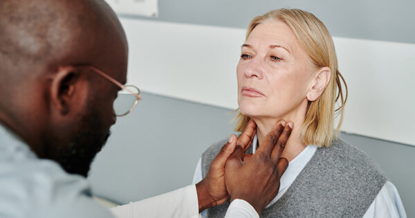Mature blond female patient having checkup of her thyroid glands by African American male endocrinologist in medical office