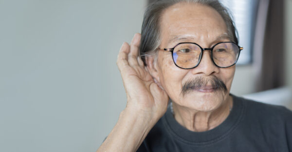 Middle age Asian man wearing eye glasses over gray background with hand over ear listening. Close up, copy space.