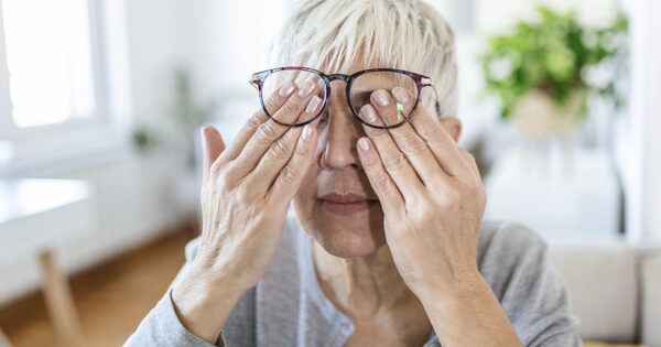 Mature woman holds glasses with diopter lenses,rubs her eyes and looks through them, the problem of myopia, vision correction