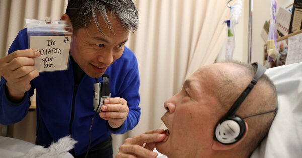 Richard Liu cares for his father who has Alzheimer's disease. He holds up a card that says "I'm RICHARD, your son."