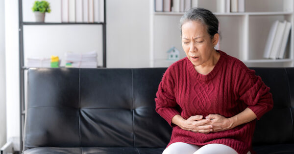 Asian senior woman suffering stomach pain sitting on sofa at home