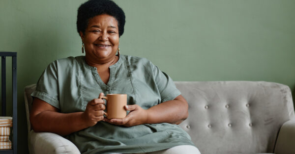 Portrait of black senior woman smiling at camera while enjoying cup of coffee at home, copy space