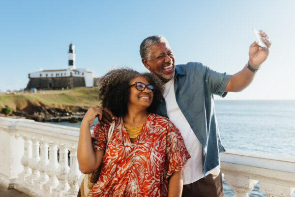 Happy elderly couple taking a selfie near the coast, with the sea and a lighthouse in the background. Retired Life at it's best.