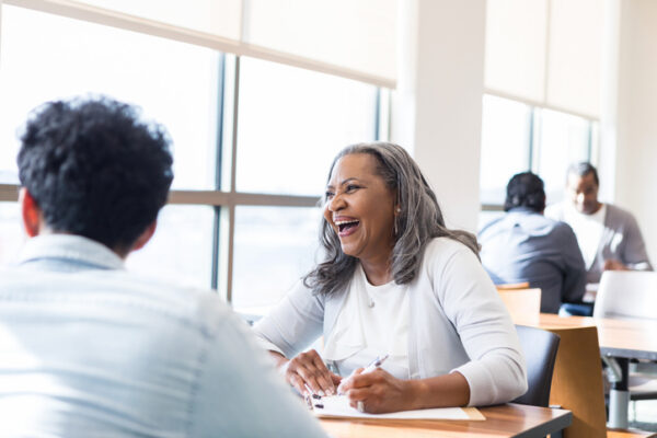 A senior adult smiles and laughs as she works with a person.
