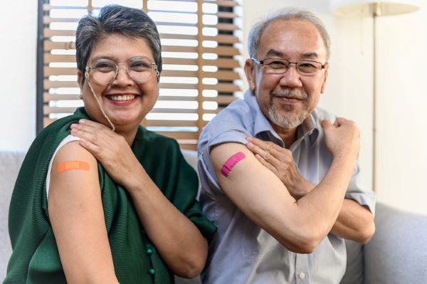 Two older adults show off their bandages after getting vaccinated.