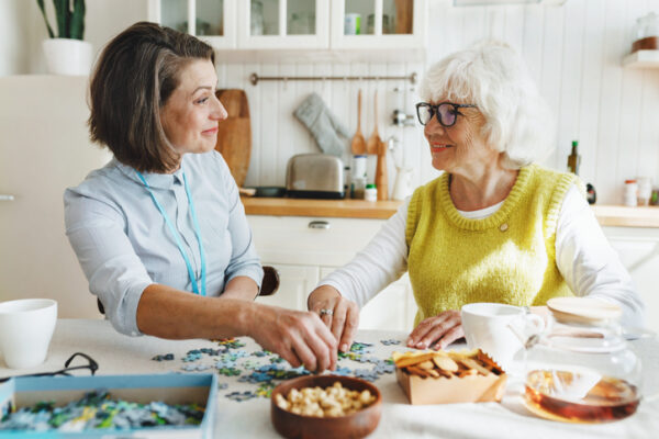Senior woman in glasses solving a puzzle with her daughter at a kitchen table